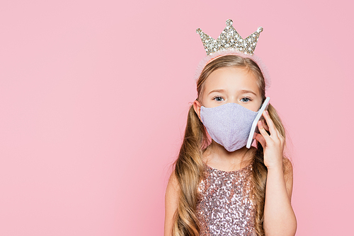girl in crown and medical mask talking on smartphone isolated on pink