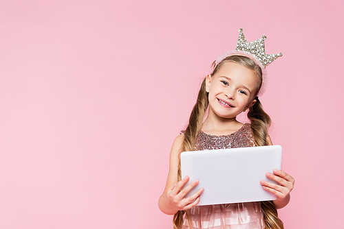 happy little girl in crown holding digital tablet isolated on pink