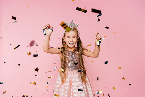 cheerful little girl in crown and dress near falling confetti on pink