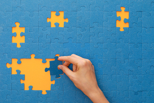 cropped view of woman putting piece of blue jigsaw puzzle on yellow background