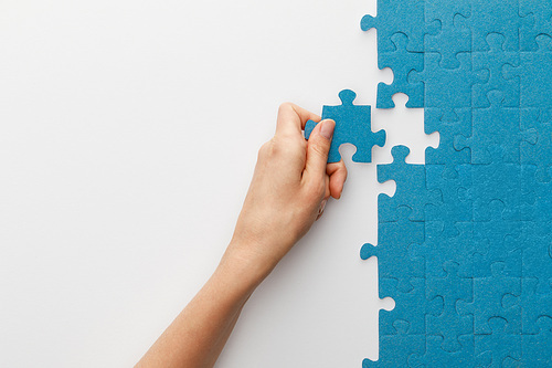 cropped view of woman attaching blue jigsaw puzzle on white background