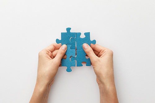 cropped view of woman holding pieces of blue jigsaw puzzle on white background