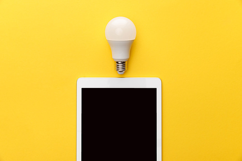 top view of light bulb and digital tablet with blank screen on yellow background