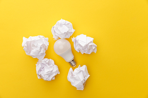 top view of light bulb between crumpled paper on yellow background