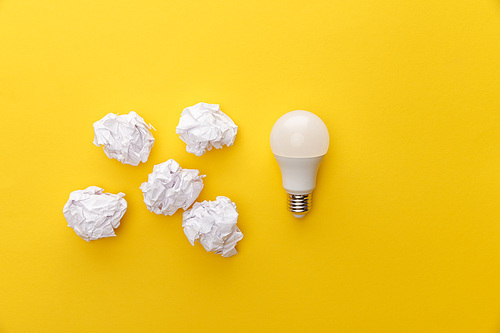 top view of light bulb near crumpled paper on yellow background