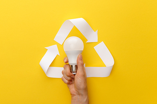 cropped view of woman holding light bulb under paper craft triangle on yellow background