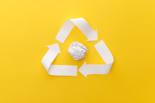 top view of white triangle with crumpled paper on yellow background