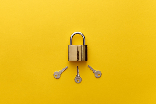 top view of metal padlock with keys on yellow background
