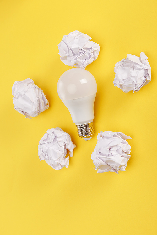 top view of crumpled paper around light bulb on yellow background