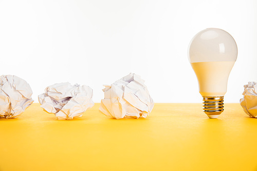 crumpled paper near light bulb on yellow surface isolated on white