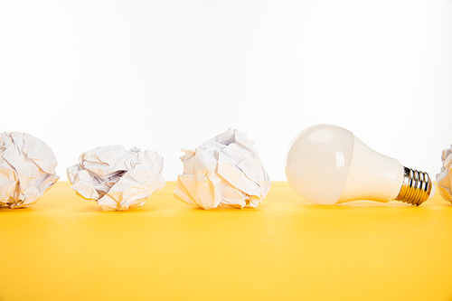 light bulb near crumpled paper on yellow surface isolated on white