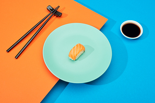 fresh nigiri with salmon near soy sauce and chopsticks on blue and orange surface