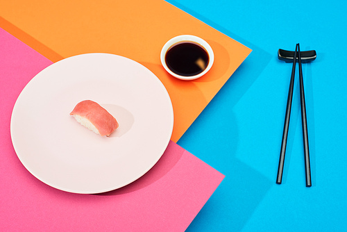 fresh nigiri with tuna near soy sauce and chopsticks on pink, blue, orange surface