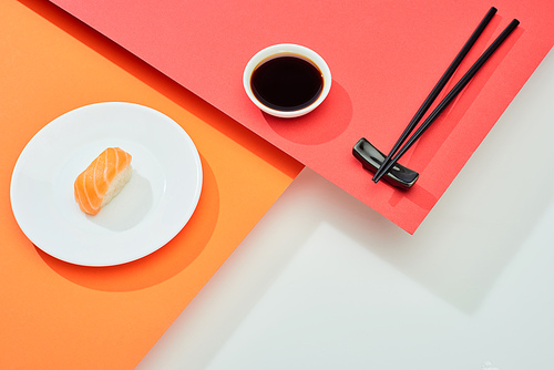 fresh nigiri with salmon near soy sauce and chopsticks on red, orange, white surface