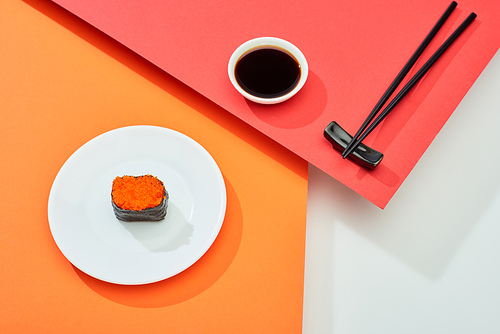 fresh nigiri with red caviar near soy sauce and chopsticks on red, orange, white surface