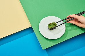 cropped view of woman eating fresh nigiri with seaweed with chopsticks on multicolored surface