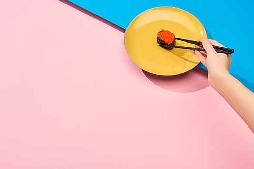 cropped view of woman eating fresh nigiri with red caviar with chopsticks on blue, pink surface