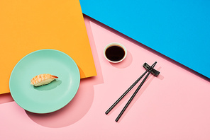 fresh nigiri with shrimp near soy sauce and chopsticks on blue, pink, orange surface