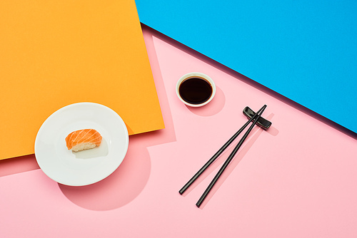 fresh nigiri with salmon near soy sauce and chopsticks on blue, pink, orange surface