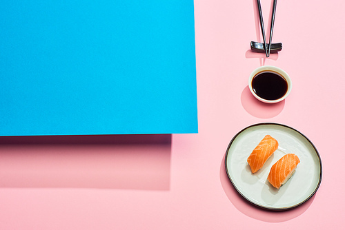 fresh nigiri with salmon near soy sauce and chopsticks on blue, pink background