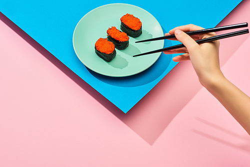 cropped view of woman eating fresh nigiri with red caviar on blue, pink background