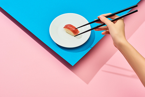 cropped view of woman eating fresh nigiri with tuna with chopsticks on blue, pink background