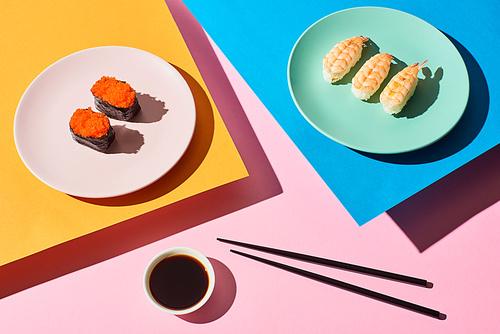 top view of fresh nigiri with shrimps and red caviar near soy sauce and chopsticks on blue, pink, orange background