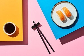top view of fresh nigiri with salmon near soy sauce and chopsticks on blue, pink, orange background