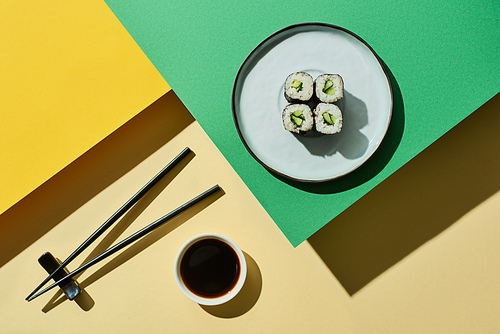 top view of fresh nigiri with cucumber near soy sauce and chopsticks on green and yellow surface