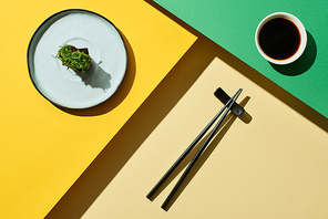top view of fresh nigiri with seaweed near soy sauce and chopsticks on green and yellow surface