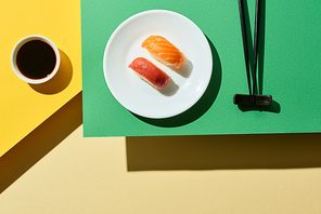 top view of fresh nigiri with salmon and tuna near soy sauce and chopsticks on green and yellow surface
