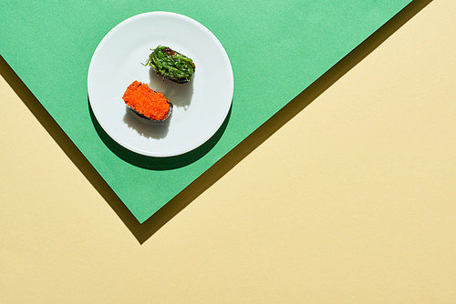 top view of fresh nigiri with red caviar and seaweed on green and yellow surface