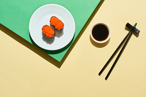top view of fresh nigiri with red caviar near soy sauce and chopsticks on green and yellow surface