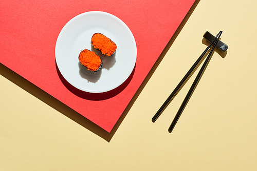 top view of fresh nigiri with red caviar near chopsticks on red and beige surface