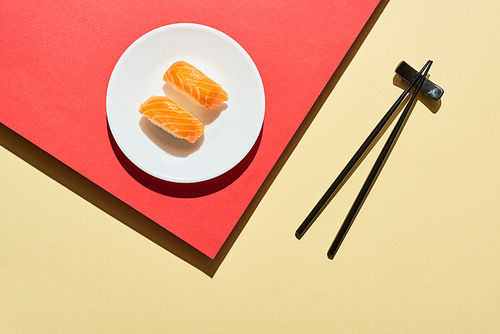top view of fresh nigiri with salmon near chopsticks on red and beige surface