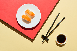 top view of fresh nigiri with salmon near soy sauce and chopsticks on red and beige surface