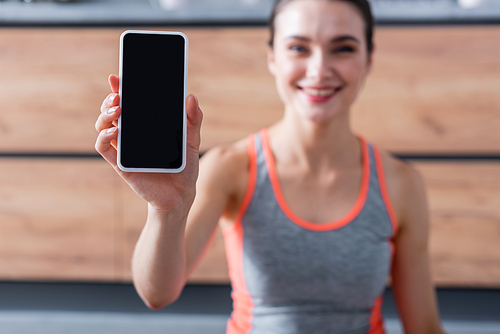 Selective focus of sportswoman showing smartphone with blank screen at home