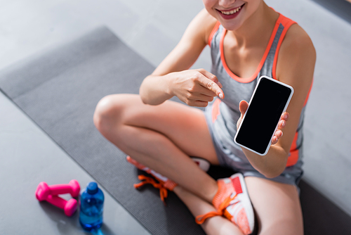 Cropped view of woman in sportswear pointing at smartphone with blank screen on fitness mat