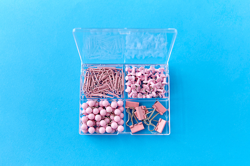 office supplies, stationery and object concept - pink pins and clips in plastic pox on blue background