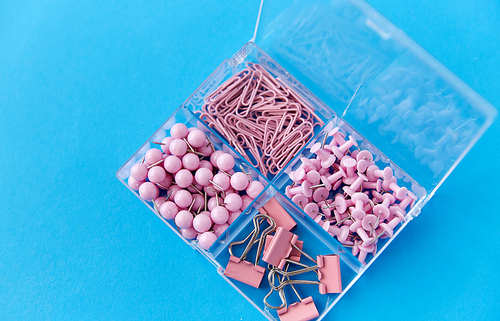 office supplies, stationery and object concept - pink pins and clips in plastic pox on blue background