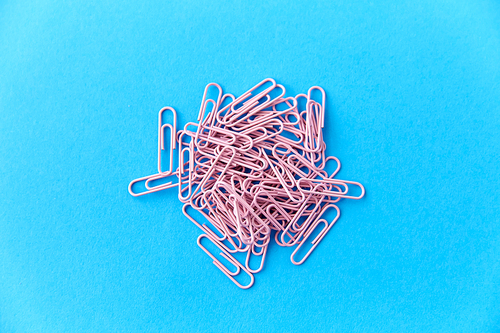 office supplies, stationery and object concept - heap of pink clips on blue background