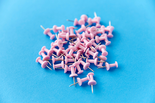 office supplies, stationery and object concept - heap of pink pins on blue background