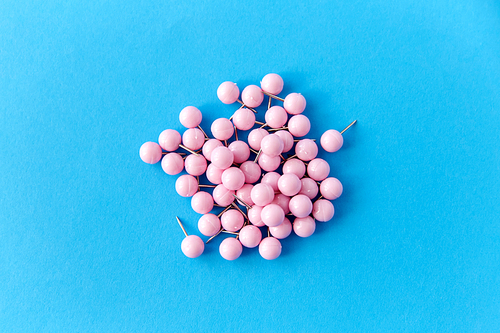 office supplies, stationery and object concept - heap of pink pins on blue background