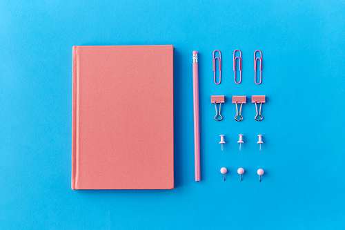 office supplies, stationery and object concept - pink notebook, pins, clips and pencil on blue background