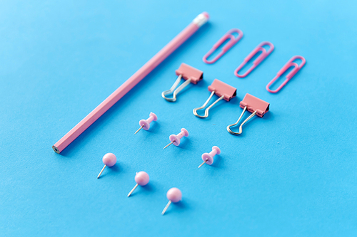 office supplies, stationery and object concept - pink pencil, pins and clips on blue background