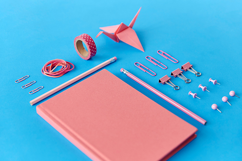 office supplies, stationery and object concept - pink notebook, pins, clips and pencils on blue background