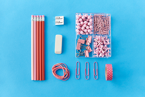 office supplies, stationery and object concept - pink pencil, pins and clips on blue background