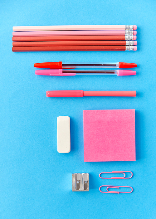 office supplies, stationery and object concept - pink sticky notes, clips, pens with pencils and eraser on blue background