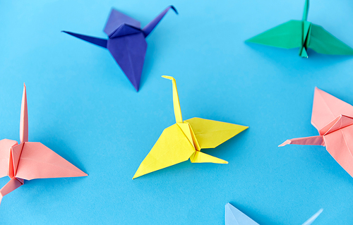 craft, hobby and creativity concept - close up of multicolored origami paper cranes on blue background