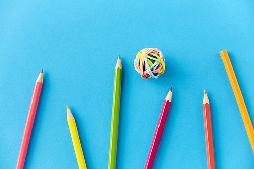 artistic tools, drawing, creativity and object concept - coloring pencils and rubber bands on blue background